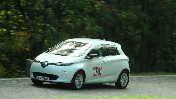 Ein weißer Renault Zoe fährt auf einer Straße mit Bäumen im Hintergrund.