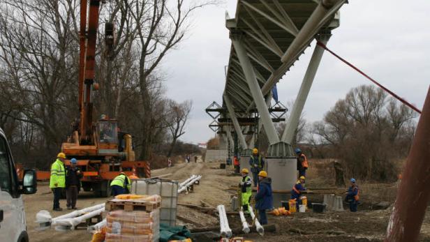 Bauarbeiter errichten eine Brücke mit Hilfe eines Krans.