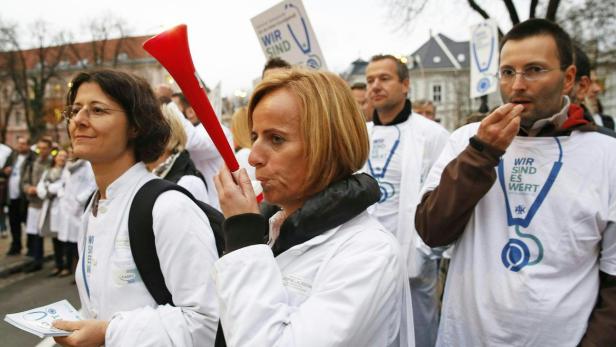 Ärzte demonstrieren mit Tröten und Schildern für bessere Arbeitsbedingungen.
