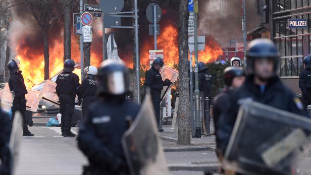 Polizisten stehen mit Schutzschilden vor einem brennenden Auto in der Klingerstraße.