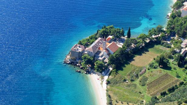 Luftaufnahme eines Klosters auf einer bewaldeten Halbinsel mit Strand.