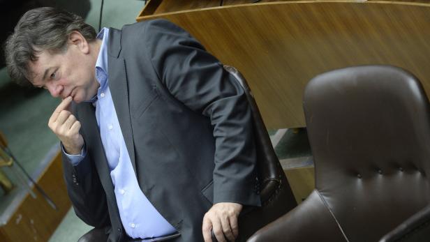 Ein Mann im Anzug sitzt nachdenklich da und berührt sein Gesicht.