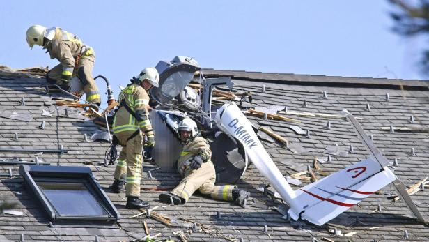 Ein Flugzeug ist in das Dach eines Hauses gestürzt, während Feuerwehrleute vor Ort sind.