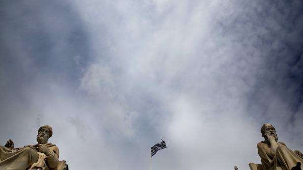 Statuen und eine griechische Flagge vor einem bewölkten Himmel.