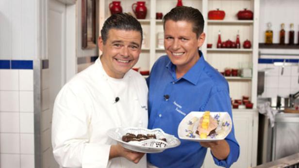 Zwei Köche präsentieren in einer Küche Desserts auf Tellern.