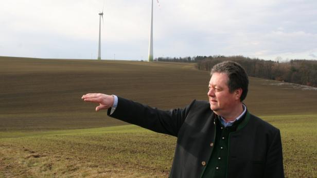 Ein Mann in Tracht deutet auf Windräder in einer ländlichen Gegend.