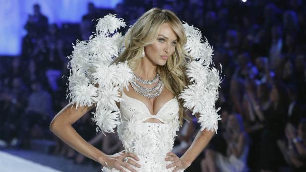Ein Model mit blonden Haaren trägt ein weißes Federkostüm und eine Halskette auf dem Laufsteg.