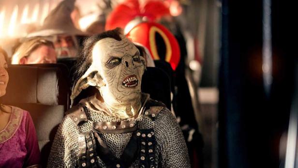 Ein Mann in einem Ork-Kostüm sitzt in einem Bus oder Zug.