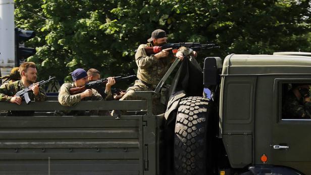 Soldaten in Tarnkleidung sitzen auf der Ladefläche eines Militärfahrzeugs und zielen mit Gewehren.