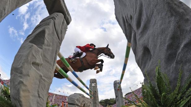Eine Reiterin springt mit ihrem Pferd über ein Hindernis vor einer Zuschauertribüne.