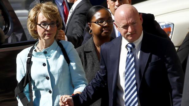 Gabrielle Giffords und Mark Kelly halten Händchen, begleitet von einer weiteren Person.