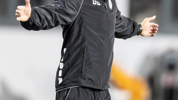 Ein Fußballtrainer gestikuliert während eines Spiels am Spielfeldrand.
