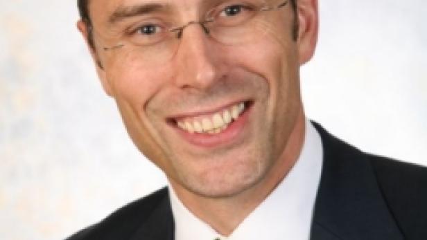 Ein lächelnder Mann mit Brille, Anzug und hellgrüner Krawatte.
