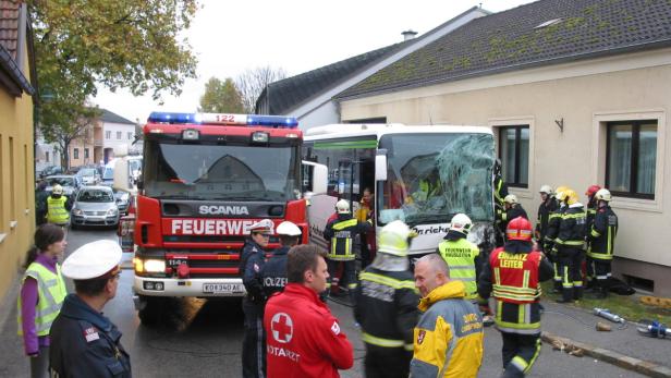Ein Feuerwehrwagen und ein Bus mit zerbrochener Windschutzscheibe stehen auf der Straße, umgeben von Einsatzkräften.