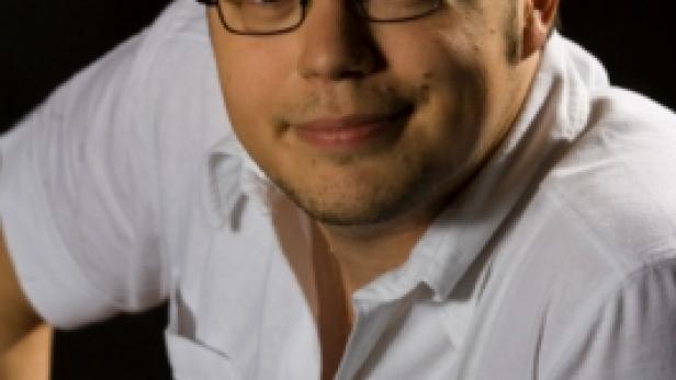Ein Mann mit Brille und weißem Hemd lächelt in die Kamera.
