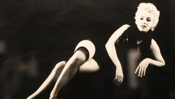 Marilyn Monroe posiert in einem schwarzen Kleid und Strapsen.