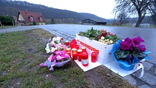 Blumen, Kerzen und eine beschriftete Kiste stehen am Straßenrand als Gedenkstätte.