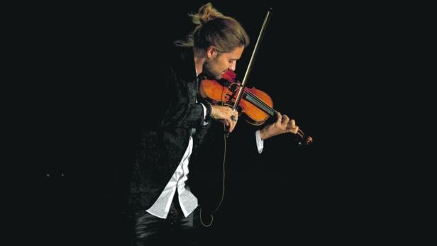 Ein Mann mit Zopf spielt auf einer Geige vor einem dunklen Hintergrund.