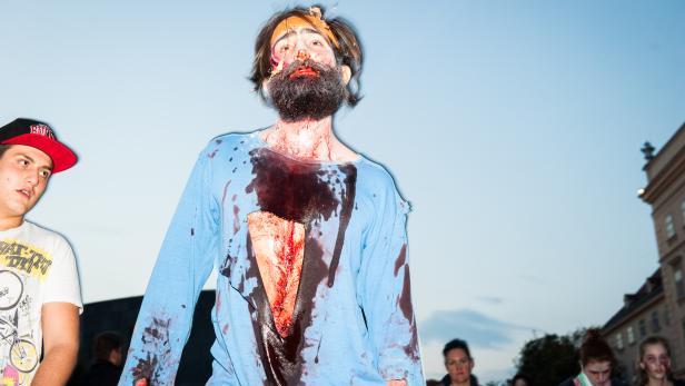 Ein Mann mit Bart und blutigem Make-up, möglicherweise ein Zombie, steht im Freien.