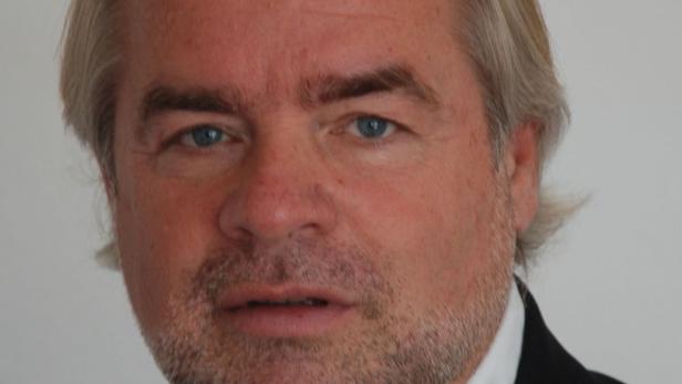 Porträt eines Mannes mit graumeliertem Haar und Bartstoppeln.