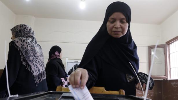 Eine Frau mit Kopftuch wirft einen Stimmzettel in eine Wahlurne.