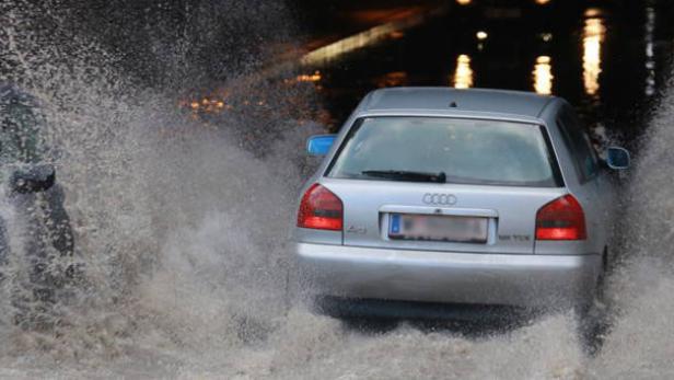 67.655.252.jpg Autos fahren durch eine überflutete Unterführung, wobei das Wasser hochspritzt.