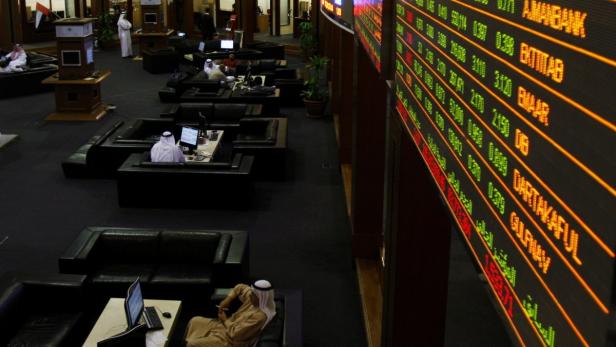 Blick in einen dunklen Raum mit Männern in traditioneller Kleidung vor Computern und einer Anzeigetafel.