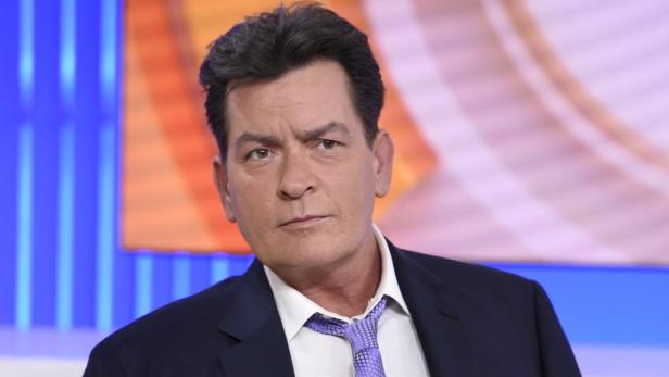 Porträt von Charlie Sheen mit Anzug und Krawatte vor einem farbigen Hintergrund.