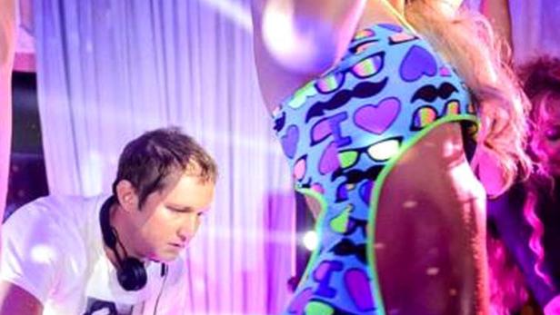 Eine Frau im Badeanzug tanzt, während ein DJ Musik auflegt.