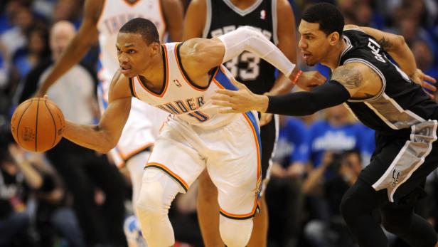 Ein Basketballspieler der Oklahoma City Thunder dribbelt den Ball, während er von einem Spieler der San Antonio Spurs verteidigt wird.