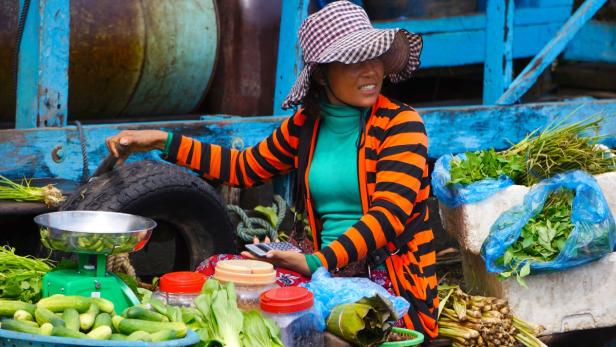 Eine Frau verkauft Gemüse und Kräuter auf einem schwimmenden Markt in Südostasien.