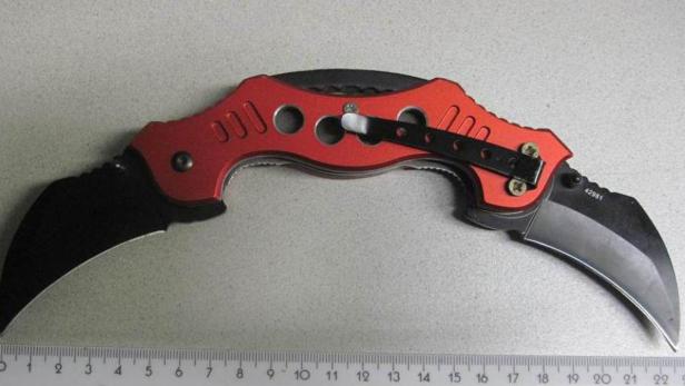 Ein rotes Doppelklingenmesser liegt auf einem Tisch neben einem Lineal.