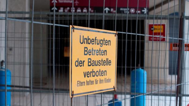 Ein gelbes Schild mit der Aufschrift „Unbefugtes Betreten der Baustelle verboten“ hängt an einem Bauzaun.