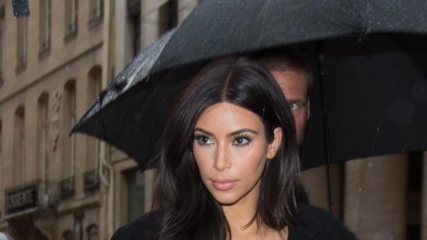 Kim Kardashian unter einem Regenschirm in einer städtischen Umgebung.