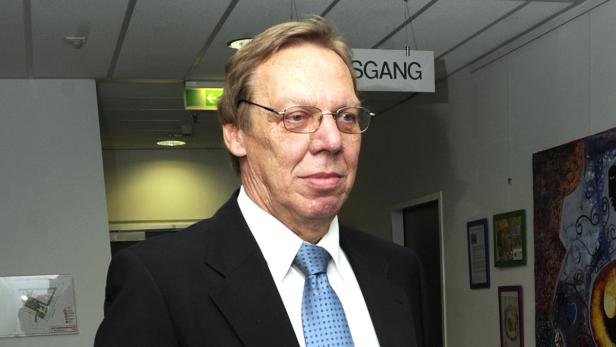 Ein Mann mit Brille und Anzug steht in einem Flur mit einem „Ausgang“-Schild.