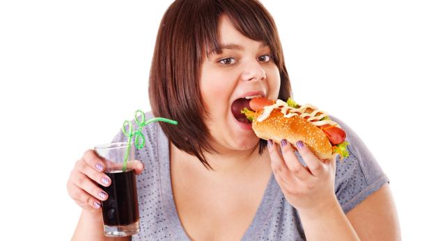 Eine Frau isst einen Hotdog und hält ein Glas Cola.