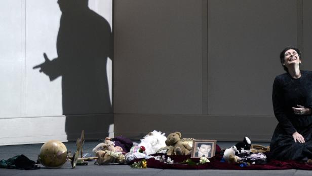 Eine Frau sitzt auf dem Boden, umgeben von Spielzeug und einem Schattenbild an der Wand.