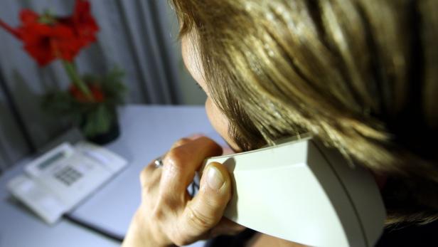 Eine Frau telefoniert mit einem weißen Telefonhörer am Ohr.