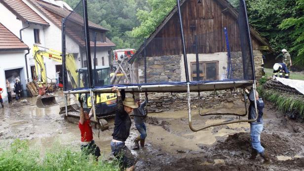 Helfer tragen ein Trampolin durch das schlammige, überflutete Gebiet nach einem Hochwasser.