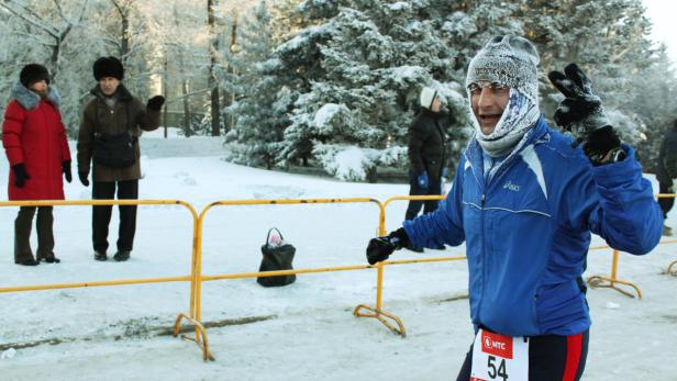 Ein Läufer mit frostbedecktem Gesicht macht bei einem Winterrennen das Victory-Zeichen.