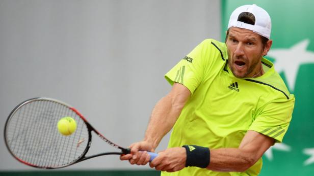 Ein Tennisspieler in einem gelben Hemd schlägt einen Ball mit seinem Schläger.