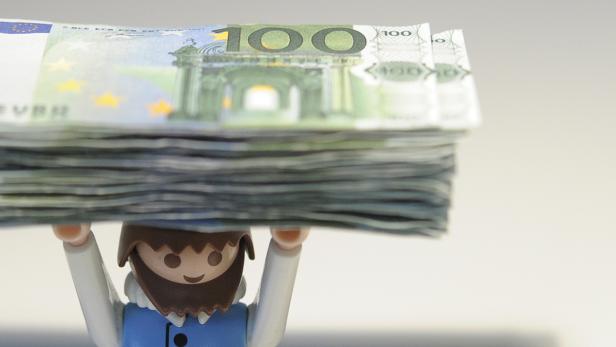 Eine Playmobilfigur stemmt einen Stapel von 100-Euro-Scheinen.
