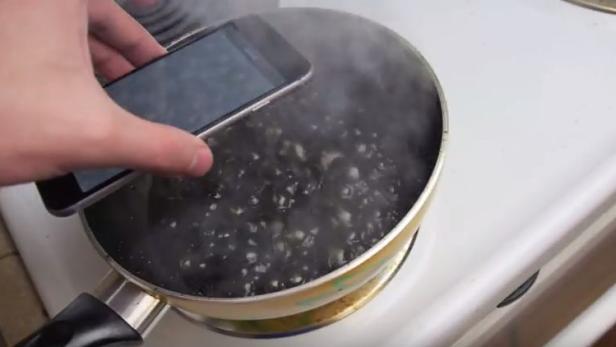 Ein Smartphone wird in einen Topf mit kochendem Wasser gehalten.