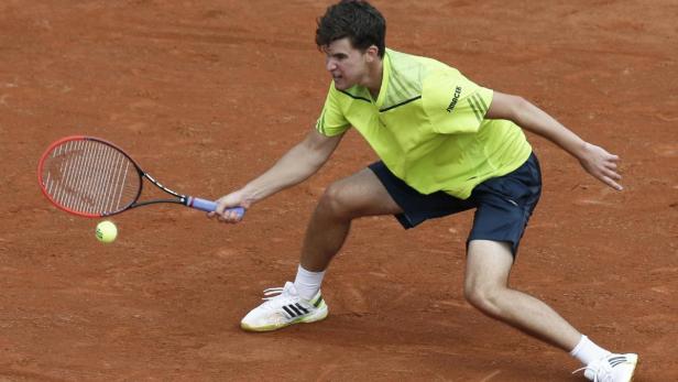 Ein Tennisspieler schlägt einen Ball auf einem Sandplatz.