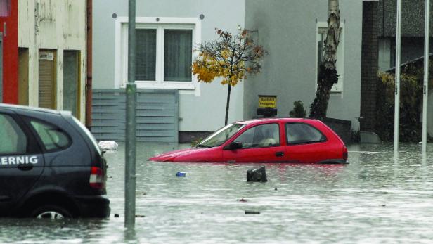 Ein rotes Auto steht im überfluteten Wasser vor Wohnhäusern.