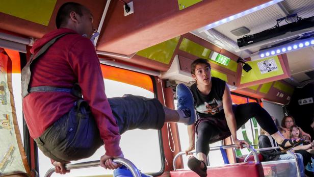 Zwei Akrobaten führen eine Performance in einem Bus vor Publikum auf.