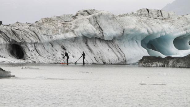 Zwei Personen paddeln auf einem See vor einem großen Gletscher.