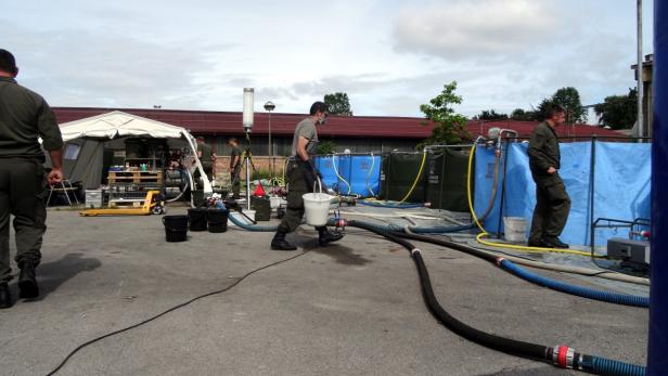 Männer in Uniform arbeiten mit Schläuchen und Wasserbehältern im Freien.