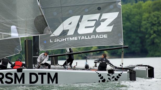 Ein Segelboot mit dem AEZ-Logo und mehreren Personen an Bord segelt auf dem Wasser.