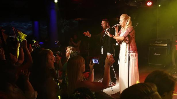 Eine Sängerin und ein Sänger treten vor Publikum auf einer Bühne auf.